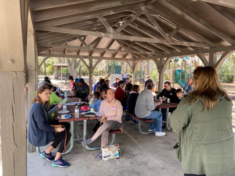 Several attendees of the Camp Kudzu Cookout sit at tables and listen to a speaker giving a presentation.